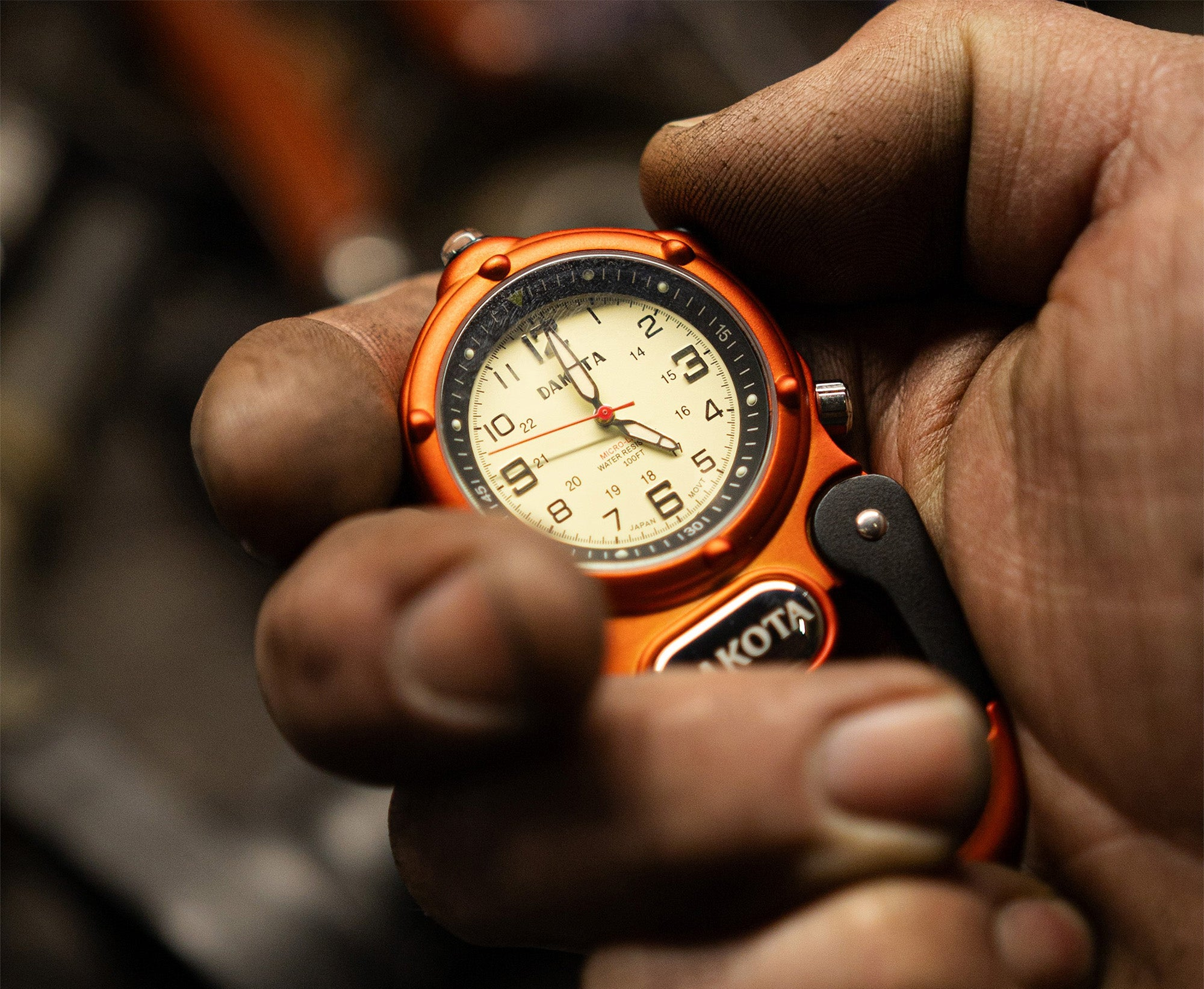 Orange Miniclip Microlight watch with a detailed face held in a hand against a blurred background