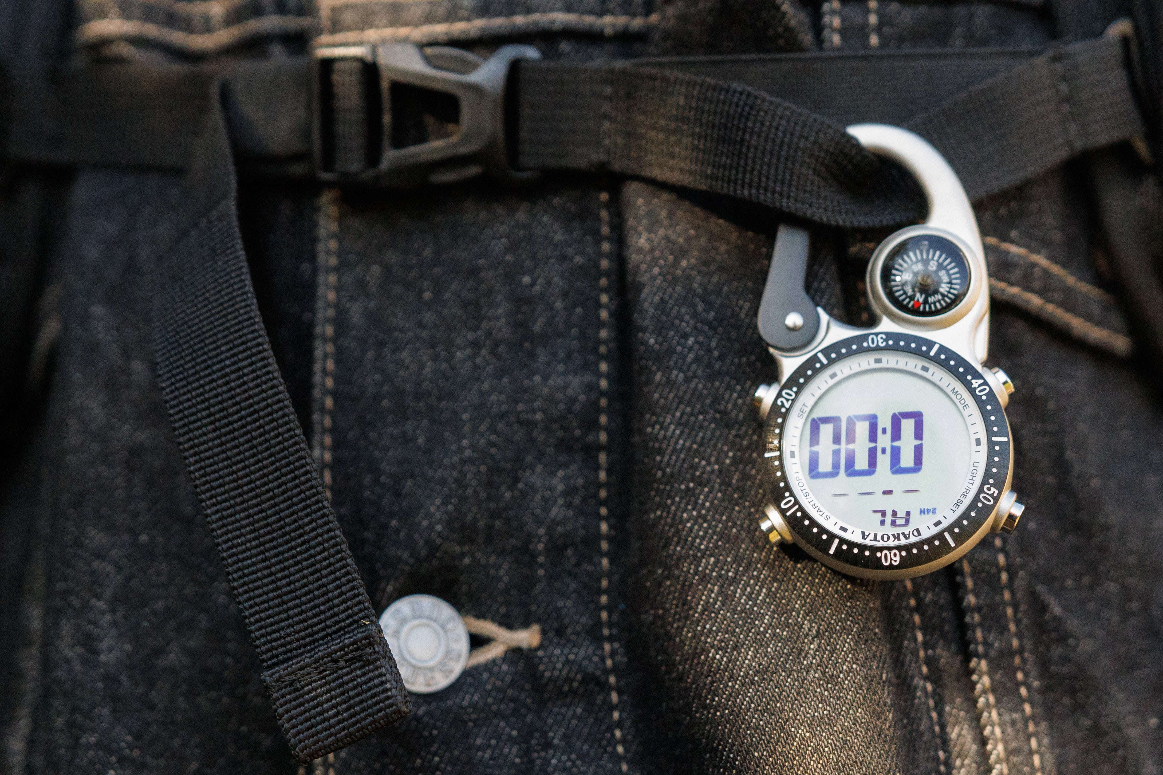 Digital Clip watch on a denim jacket, hooked onto a backpack strap.