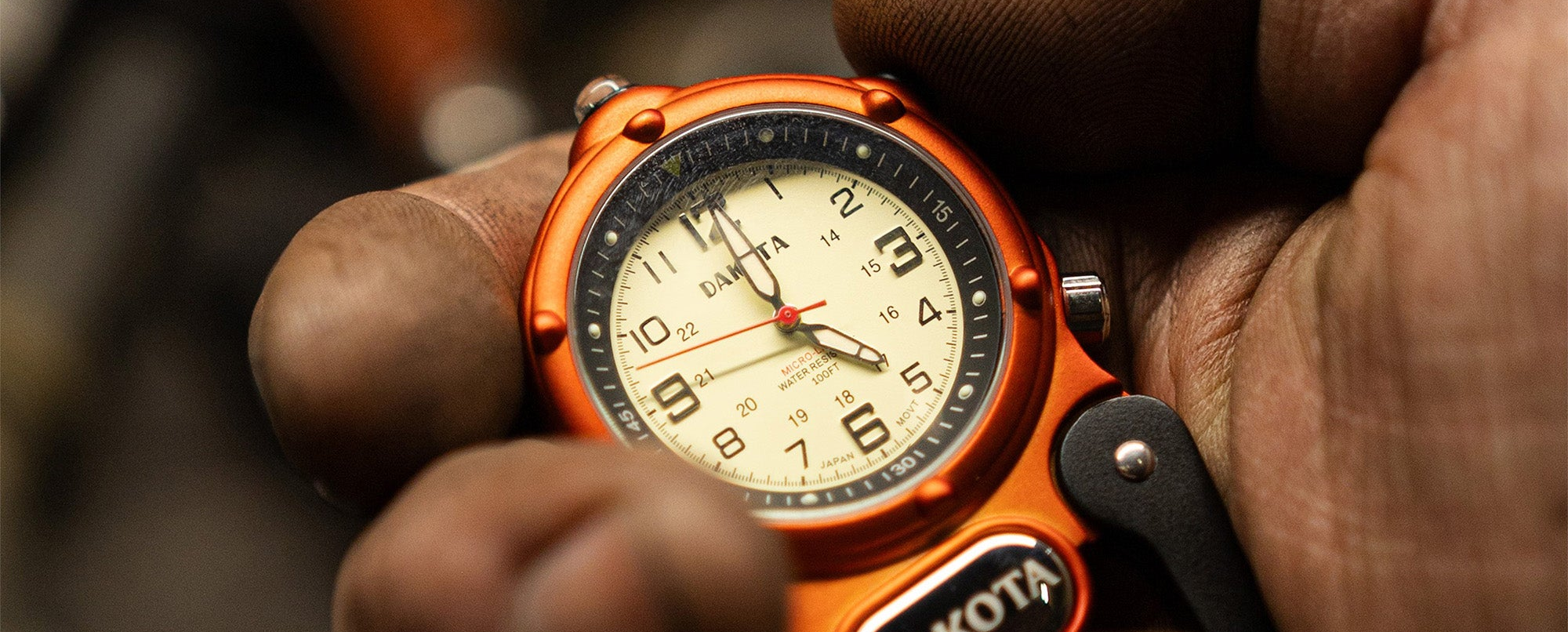 Orange Miniclip Microlight watch with a detailed face held in a hand against a blurred background