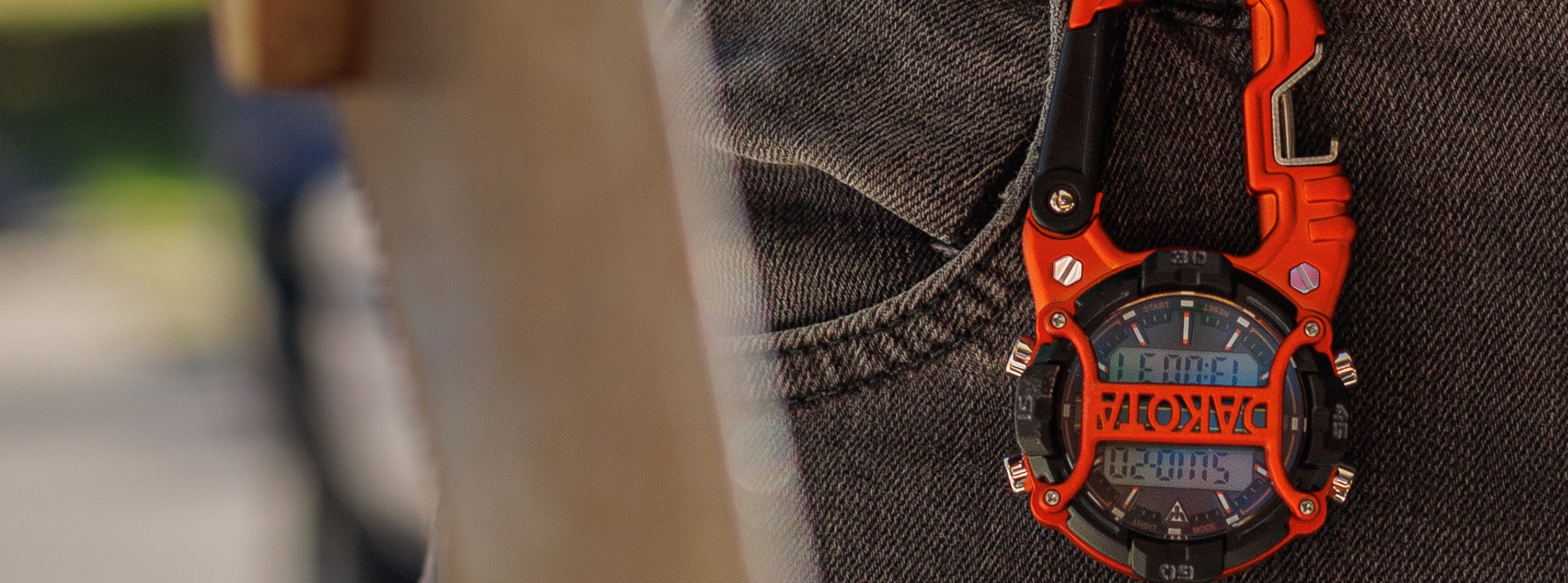 Orange and black digital bottle opener clip watch on a person's jeans with blurry background